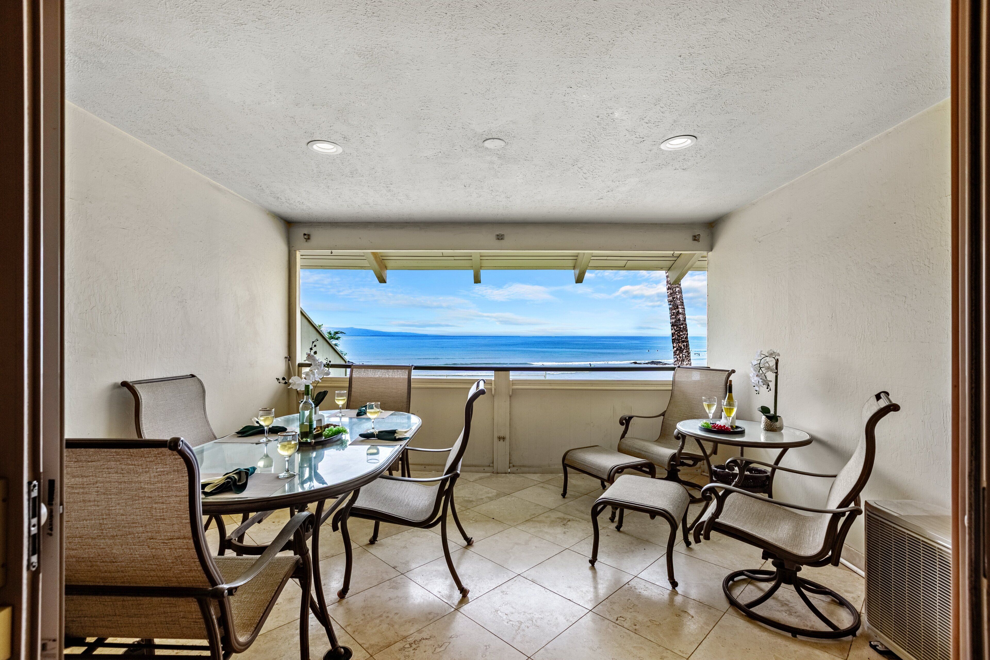 A balcony with a view of the ocean, furnished with a table and chairs, and a small table with drinks.