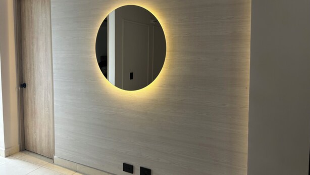 Un interior moderno con un espejo circular en una pared con textura, una puerta y un interruptor de luz.