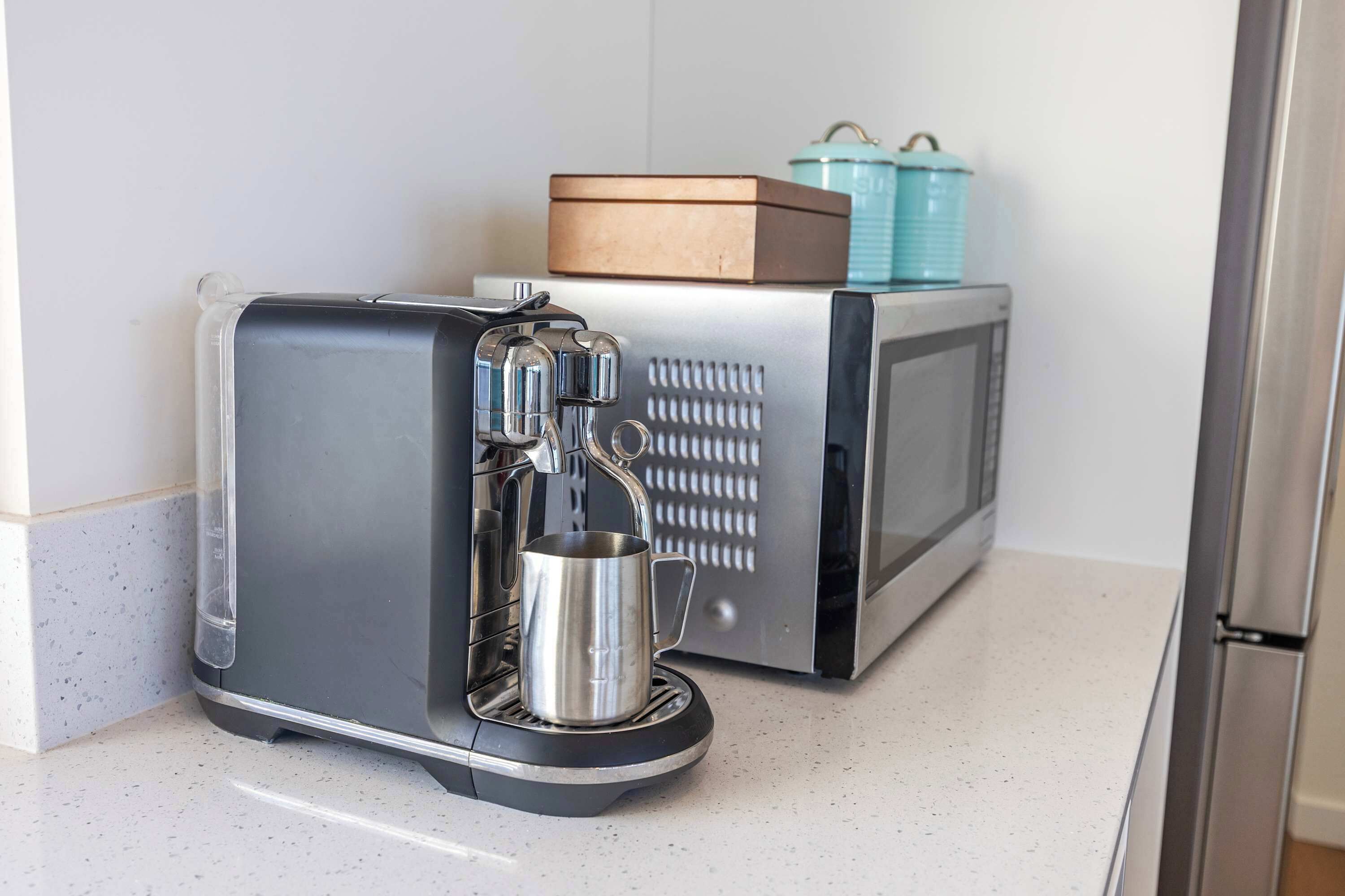 A compact kitchen with a coffee maker, a microwave, and a small cabinet with a box and a container on top.