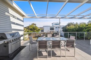 An outdoor patio with a grill, glass table, and chairs.