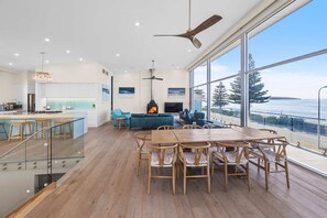 A spacious living area with a large wooden dining table, a fireplace, and a view of the ocean.