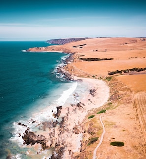 A coastal landscape with a beach, rocky shoreline, and a dirt path.