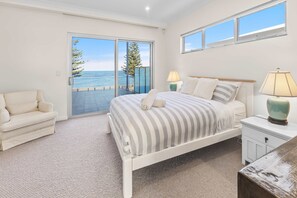 A bedroom with a bed, a chair, a nightstand, and a view of the sea through a sliding door.