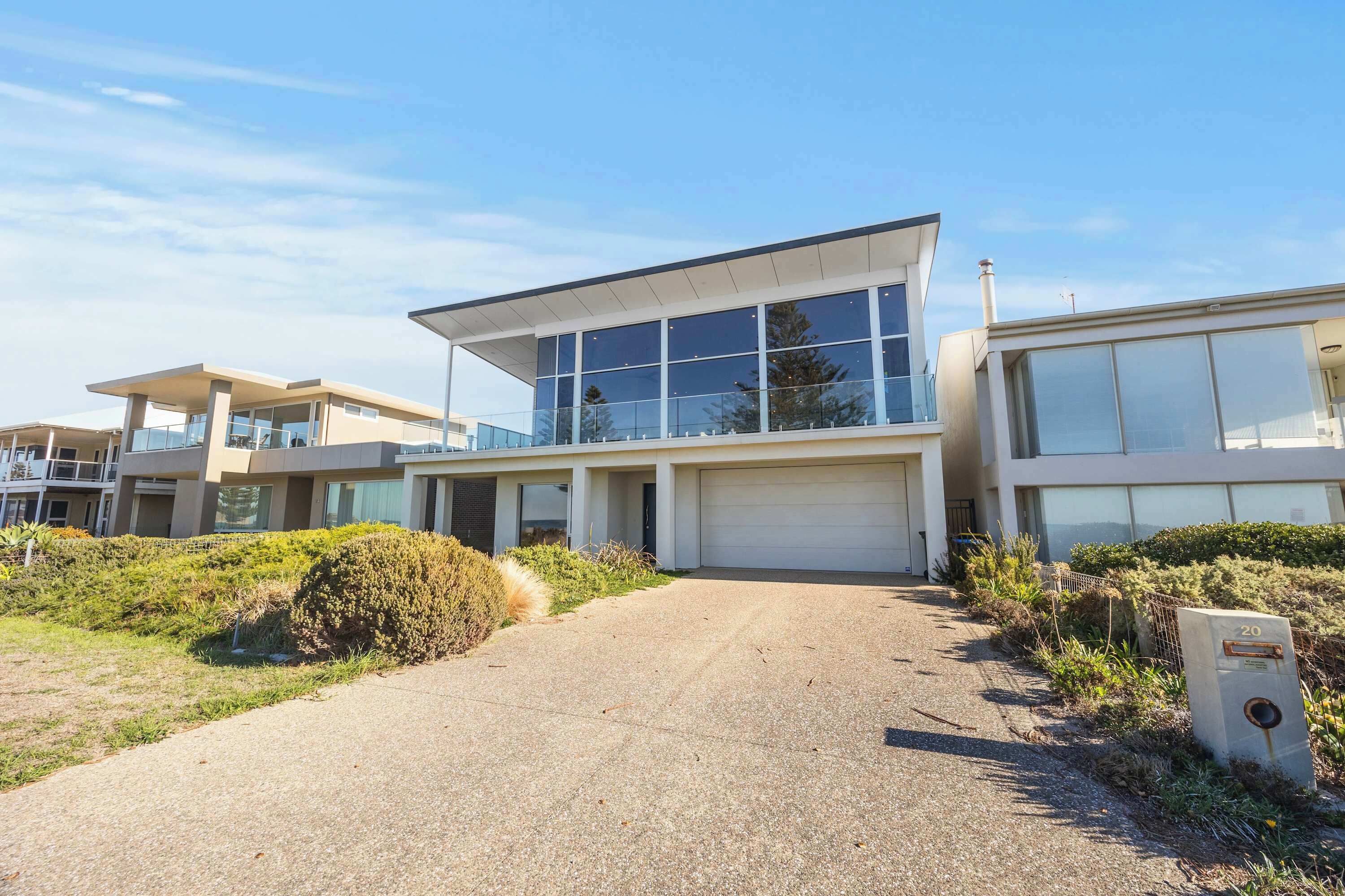 Un bâtiment moderne doté de grandes fenêtres, d’un garage et d’une allée pavée.