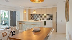 Een moderne keuken met een centraal eiland, hangende lampen en een eethoek met een houten tafel.
