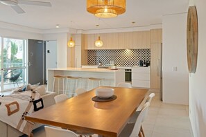 Eine moderne Küche mit einer zentralen Kochinsel, Pendelleuchten und einem Essbereich mit einem Holztisch.