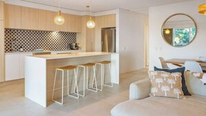 Een moderne keuken met een centraal eiland, barstoelen, hanglampen en een eethoek met een ronde spiegel en kussens.