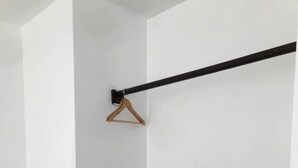 Een hoek van een kamer met een zwarte metalen stang, een houten kleerhanger en twee zwarte planken tegen een witte muur.