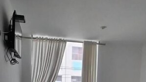 Een slaapkamer met een bed, een ventilator, een raam met gordijnen en een wandlamp.