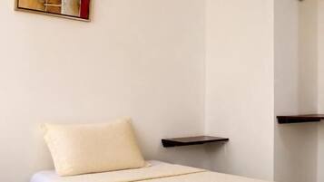 A single bed with a white bedspread, a pillow, and a neatly folded towel on the side.