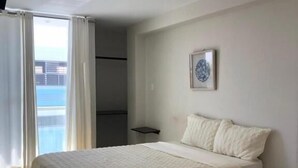 Een slaapkamer met een bed, een klein nachtkastje, een wanddecoratie en uitzicht buiten.