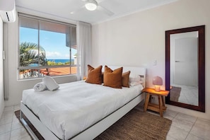 A hotel room with a bed, a nightstand, a lamp, a large window with a view, and a door.