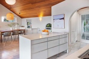 A modern kitchen with a central island, wooden ceiling, and a dining area with chairs.