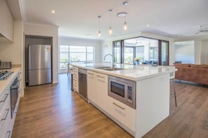 Une cuisine moderne dotée d’un îlot central, d’appareils électroménagers en acier inoxydable et donnant sur le patio extérieur.