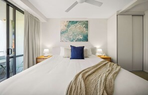 A hotel room with a large bed, two bedside tables with lamps, a ceiling fan, a sliding glass door, and a wall-mounted abstract painting. - Chic Noosa Riverside Apt with Great Facilities (Noosa Region)