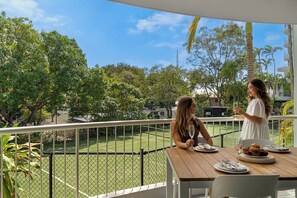 Ein Balkon mit Tisch für zwei Personen, mit Blick auf einen Tennisplatz und Grünflächen.