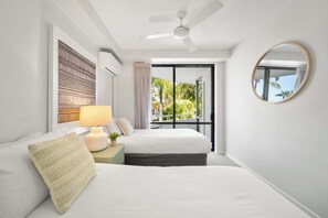 A hotel room with two beds, a ceiling fan, a large window with a view of greenery, and a round mirror on the wall. - Chic Noosa Riverside Apt with Great Facilities (Noosa Region)