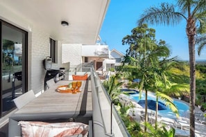 Ein modernes Haus mit Balkon und Blick auf einen Swimmingpool, umgeben von üppiger Vegetation.