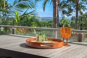 Ein Balkon mit Holztisch, einer Kupfertablett mit einer Pflanze und einem Glas.