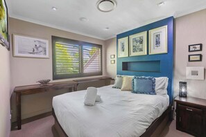 A bedroom with a bed, a desk, a window with blinds, and framed artwork on the walls. - Tropical Noosa Riverside Villa (Noosa Region)