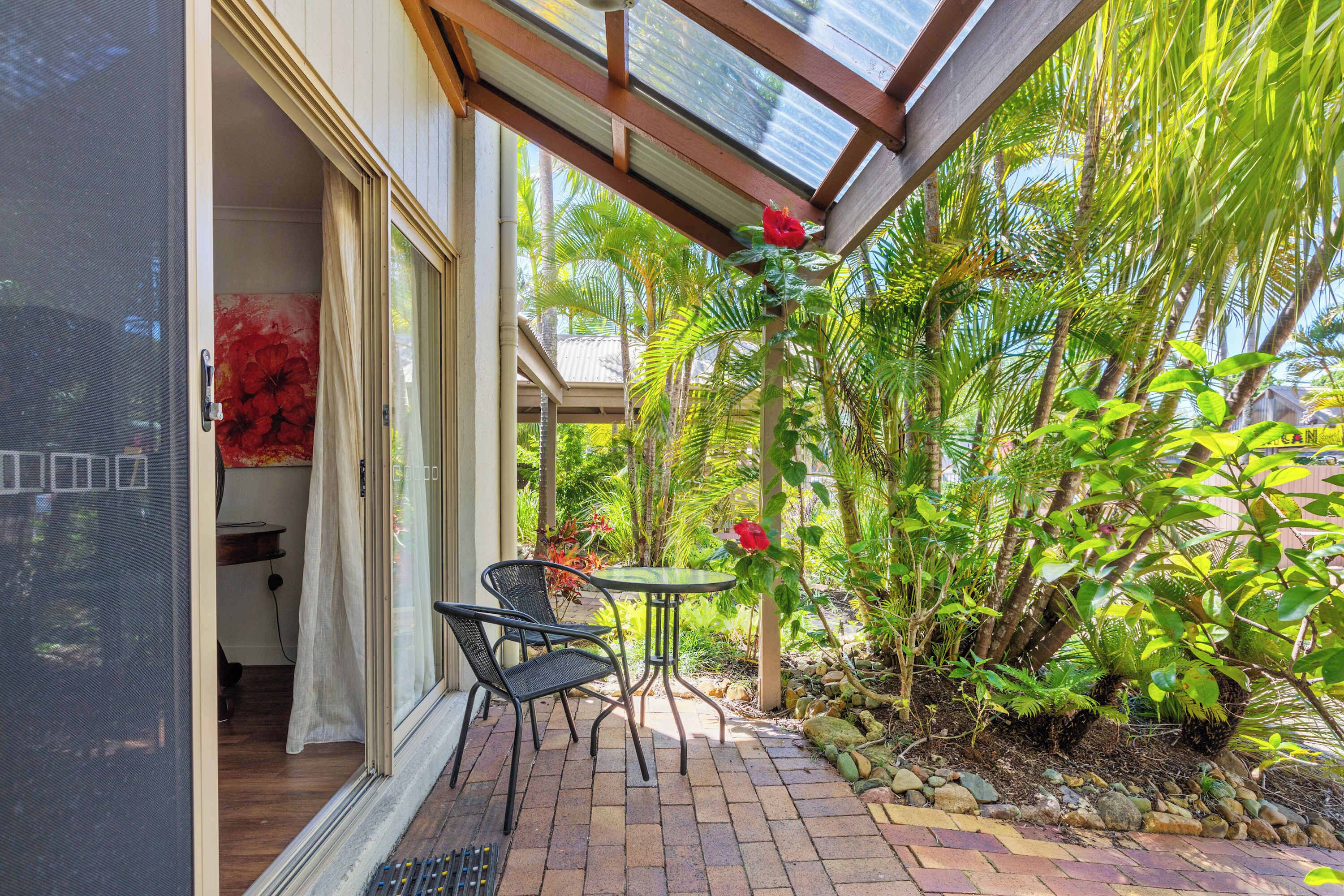 Uma área de estar coberta ao ar livre, com mesa e cadeiras, cercada por vegetação tropical exuberante e vista para o exterior.