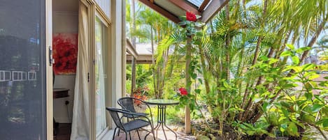 Uma área de estar coberta ao ar livre, com mesa e cadeiras, cercada por vegetação tropical exuberante e vista para o exterior.