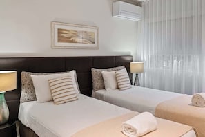A hotel room with two beds, a framed picture on the wall, an air conditioner, and a window with sheer curtains. - Noosa Hill Apt, Views, Pool, with Hasting St, Beach (Noosa Region)