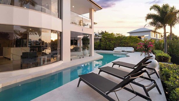 A modern house with a swimming pool, lounge chairs, and a balcony. - Luxurious Impeccably Styled Waterfront Noosa Home (Noosa Region)