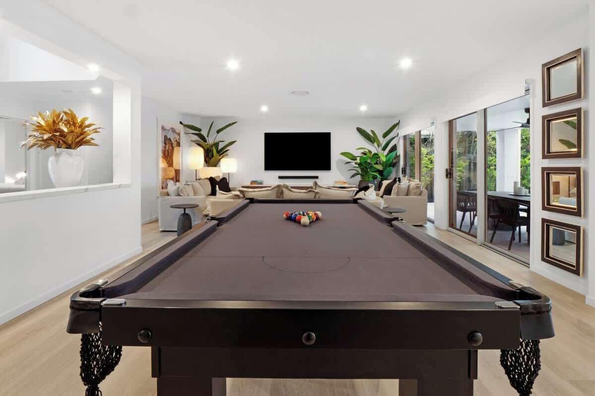 A pool table in a modern living room with a flat-screen TV, comfortable seating, and large windows.
