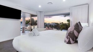 A modern hotel room with a large bed, a flat-screen TV, and a balcony with a city view. - Luxurious Impeccably Styled Waterfront Noosa Home (Noosa Region)