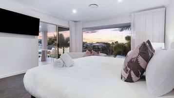 A modern hotel room with a large bed, a flat-screen TV, and a balcony with a city view.