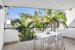 A balcony with a white table and chairs, a view of palm trees, and a clear sky. - Montpellier Riverside Apartment with Heated Pool (Noosa Region)