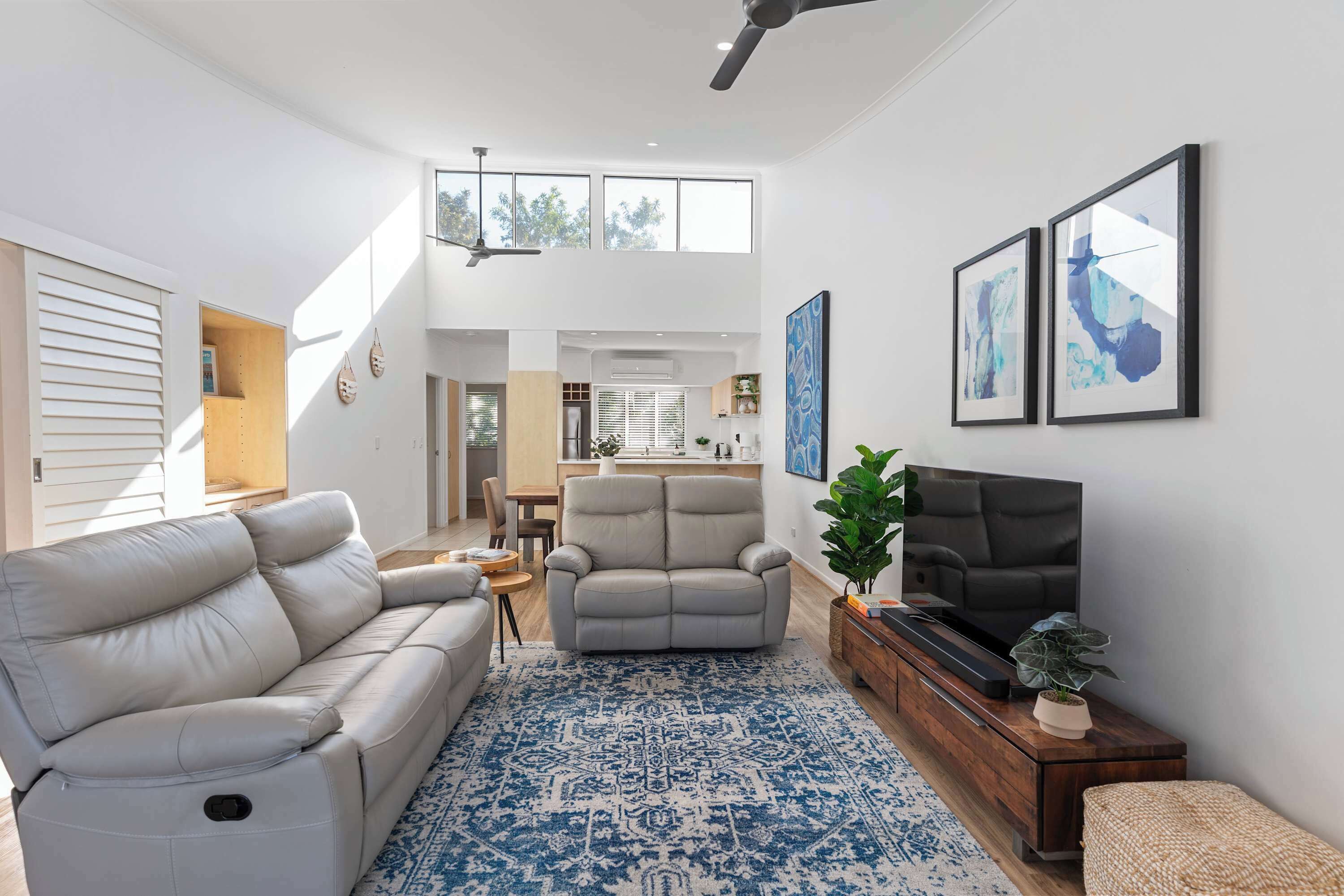 A spacious living room with a sofa, armchair, and TV, a patterned rug, and artwork on the walls.