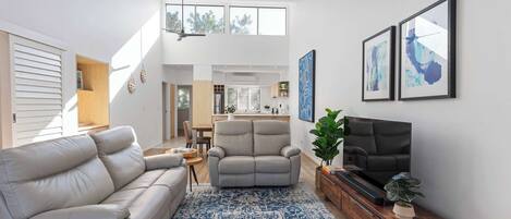 A spacious living room with a sofa, armchair, and TV, a patterned rug, and artwork on the walls.