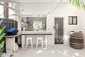 A compact kitchen with a bar area, two stools, a wooden barrel, and a door with a mesh screen. - Yarraga Tropical Escape with Pool & Private Rooftop (Noosa Region)