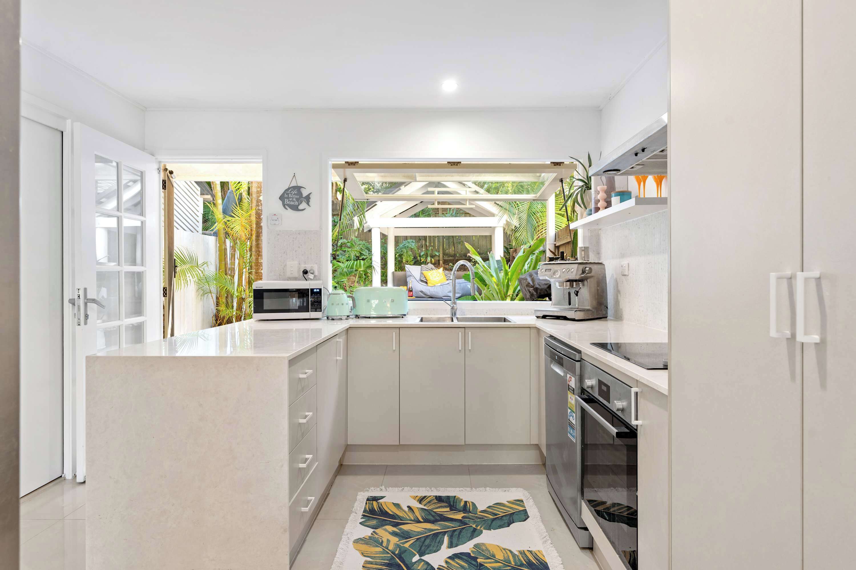 A modern kitchen with a central island, a built-in oven, and a view of a tropical garden.