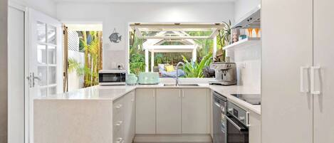 A modern kitchen with a central island, a built-in oven, and a view of a tropical garden.