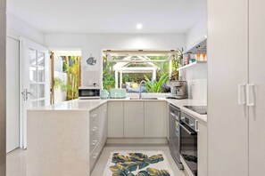 Una cuina moderna amb una illa central, forn integrat i vistes a un jardí tropical.
