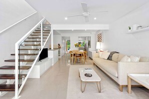 A modern living space with a staircase, a flat-screen TV, a dining area, and a sofa. - Yarraga Tropical Escape with Pool & Private Rooftop (Noosa Region)