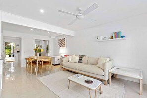A modern living room with a dining area, a ceiling fan, a sofa, a coffee table, and a bookshelf. - Yarraga Tropical Escape with Pool & Private Rooftop (Noosa Region)