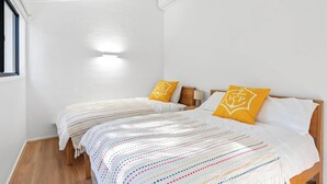 Ett hotellrum med två sängar, vita väggar, trägolv och ett fönster på vänster sida.