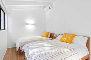 A hotel room with two beds, white walls, wooden flooring, and a window on the left. - Yarraga Tropical Escape with Pool & Private Rooftop (Noosa Region)