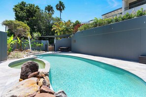 A swimming pool with a curved design, surrounded by a low wall and a variety of plants. - Yarraga Tropical Escape with Pool & Private Rooftop (Noosa Region)