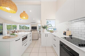 A modern kitchen with white cabinetry, a black stove, and a dining area with a TV. - Southwind in Sunrise (Noosa Region)