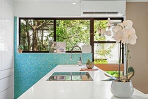 Eine moderne Küche mit einem großen Fenster, einer weißen Spüle und einer Orchidee im Blumentopf.