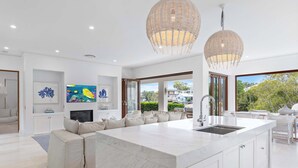 A modern kitchen with a large island, white cabinetry, and a dining area with a view. - Quintessential Noosa Waterfront Home Heated Pool (Noosa Region)