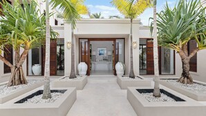 A modern building with a central entrance, surrounded by palm trees and white planters. - Quintessential Noosa Waterfront Home Heated Pool (Noosa Region)