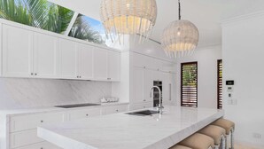 A modern kitchen with white cabinetry, a marble island, and pendant lighting. - Quintessential Noosa Waterfront Home Heated Pool (Noosa Region)