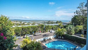 A pool area with a view of the ocean, surrounded by greenery and parked cars. - "The Outlook" Views, Pool & Walk to Main Beach (Noosa Region)