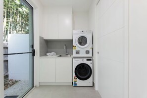 Ein kleiner Waschbereich mit Waschmaschine und Trockner, einem Waschbecken und einer gefliesten Rückwand.